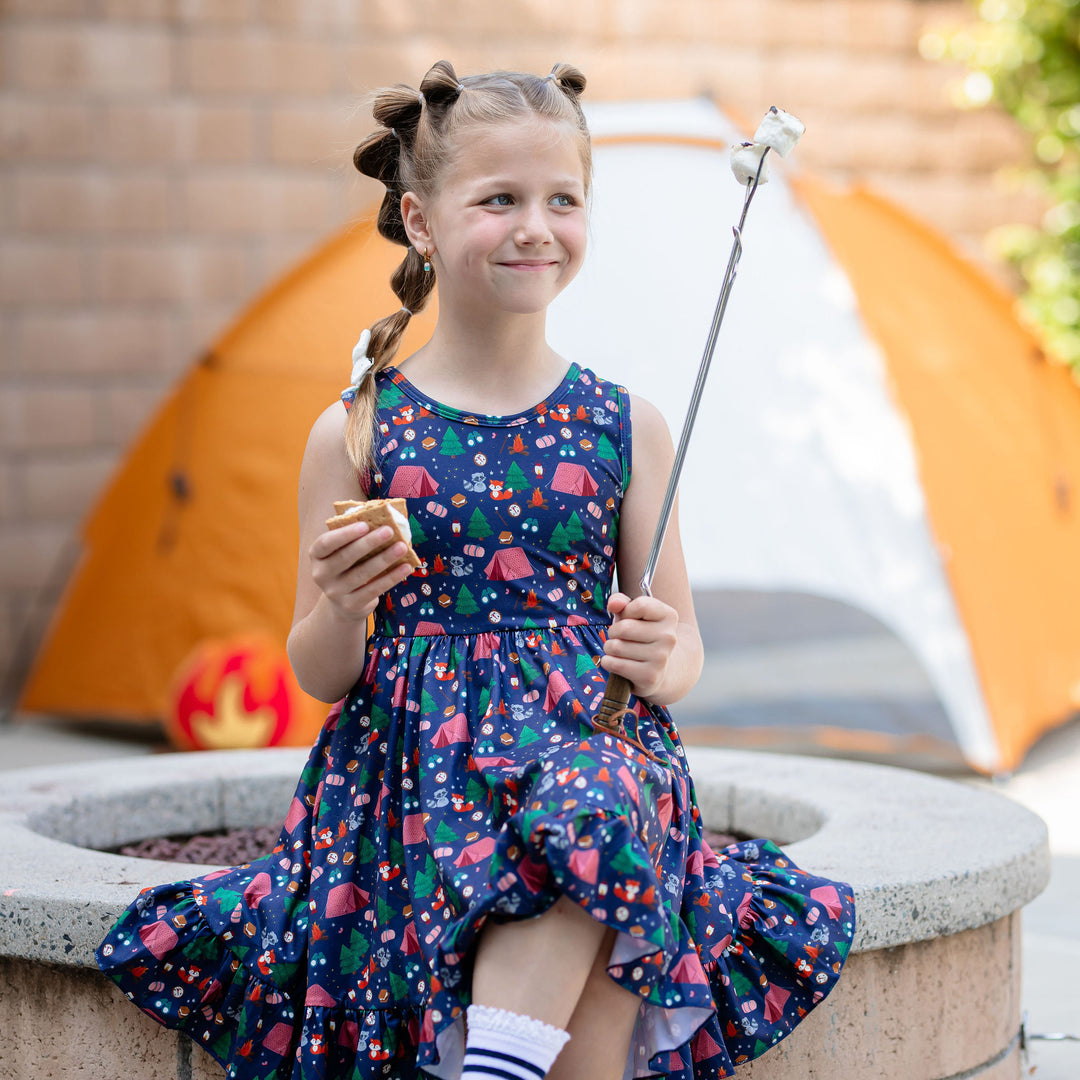 little girl sitting at campsite roasting marshmallows for smores wearing cute camping themed dress
