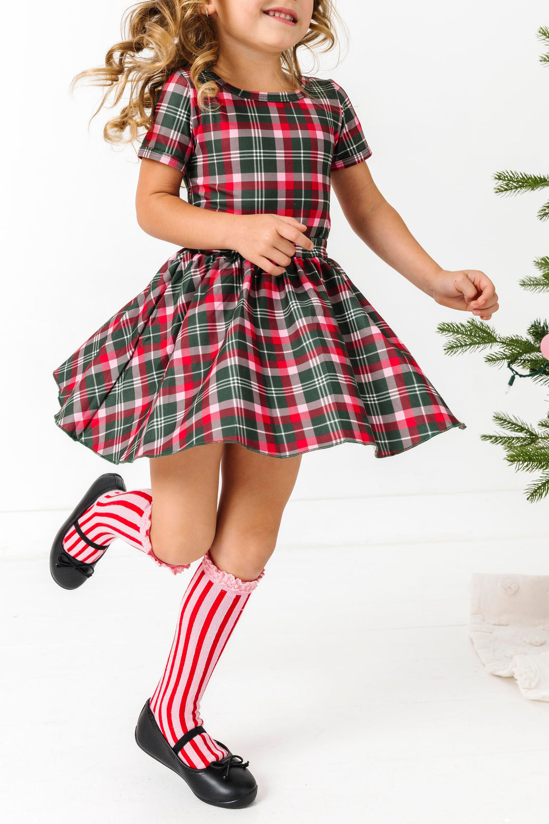 girl twirling in classic Christmas plaid top and skirt paired with pink and red striped knee high socks with lace trim