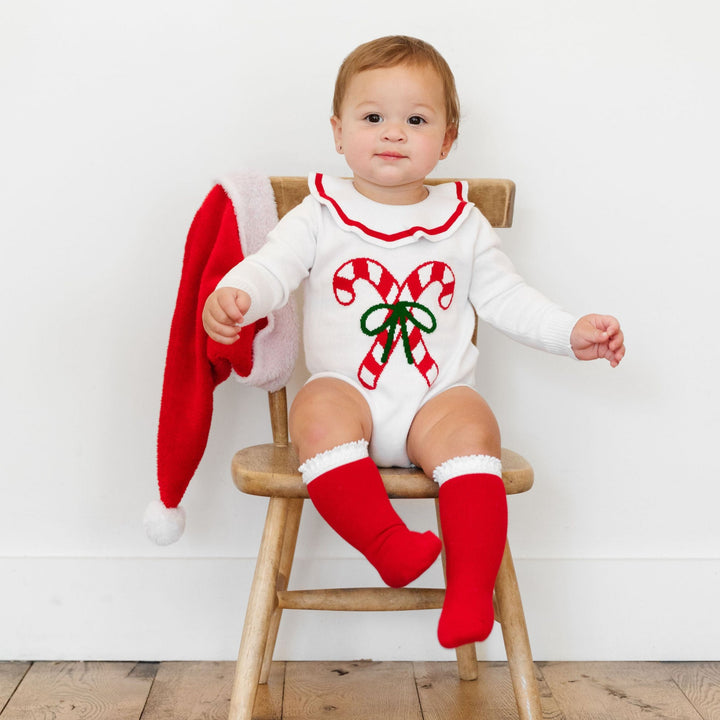 baby girl wearing candy cane knit romper with lace trim knee high socks for christmas
