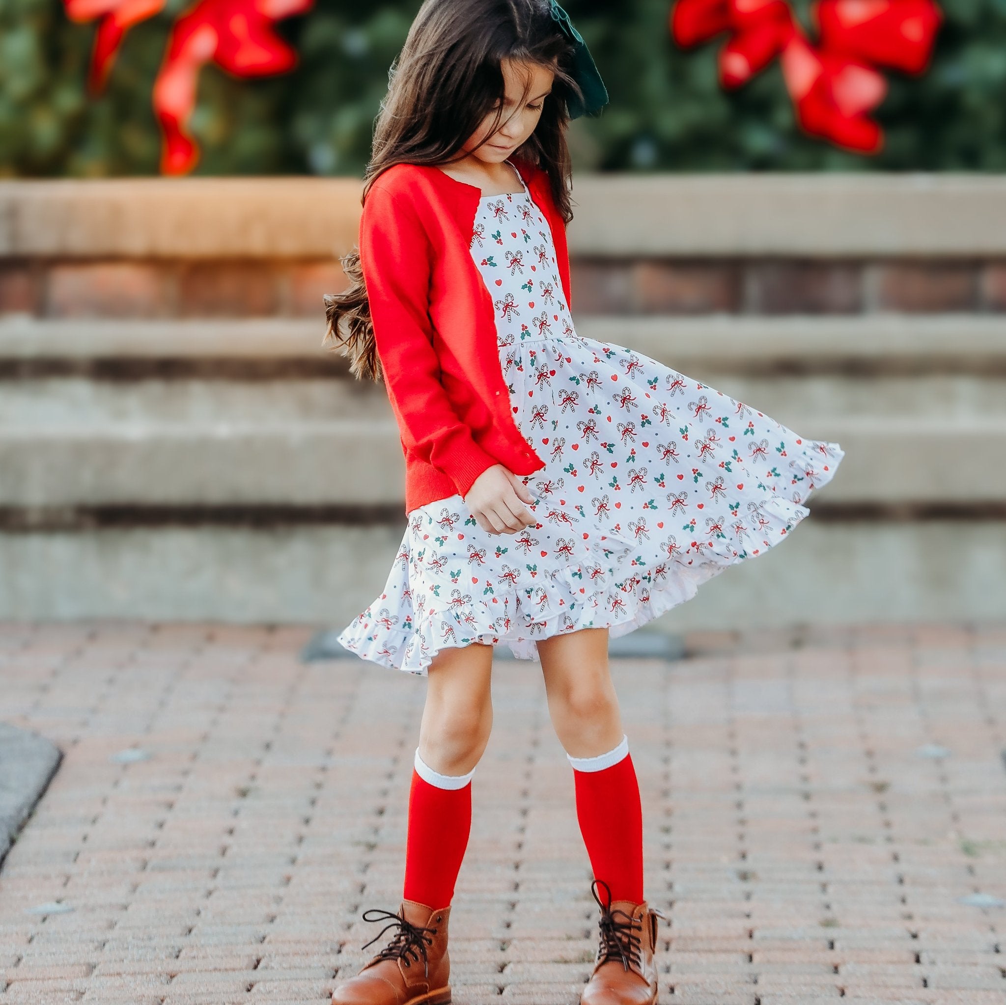 girl in christmas outfit of candy cane dress and red sparkle cardigan and red knee highs with white trim