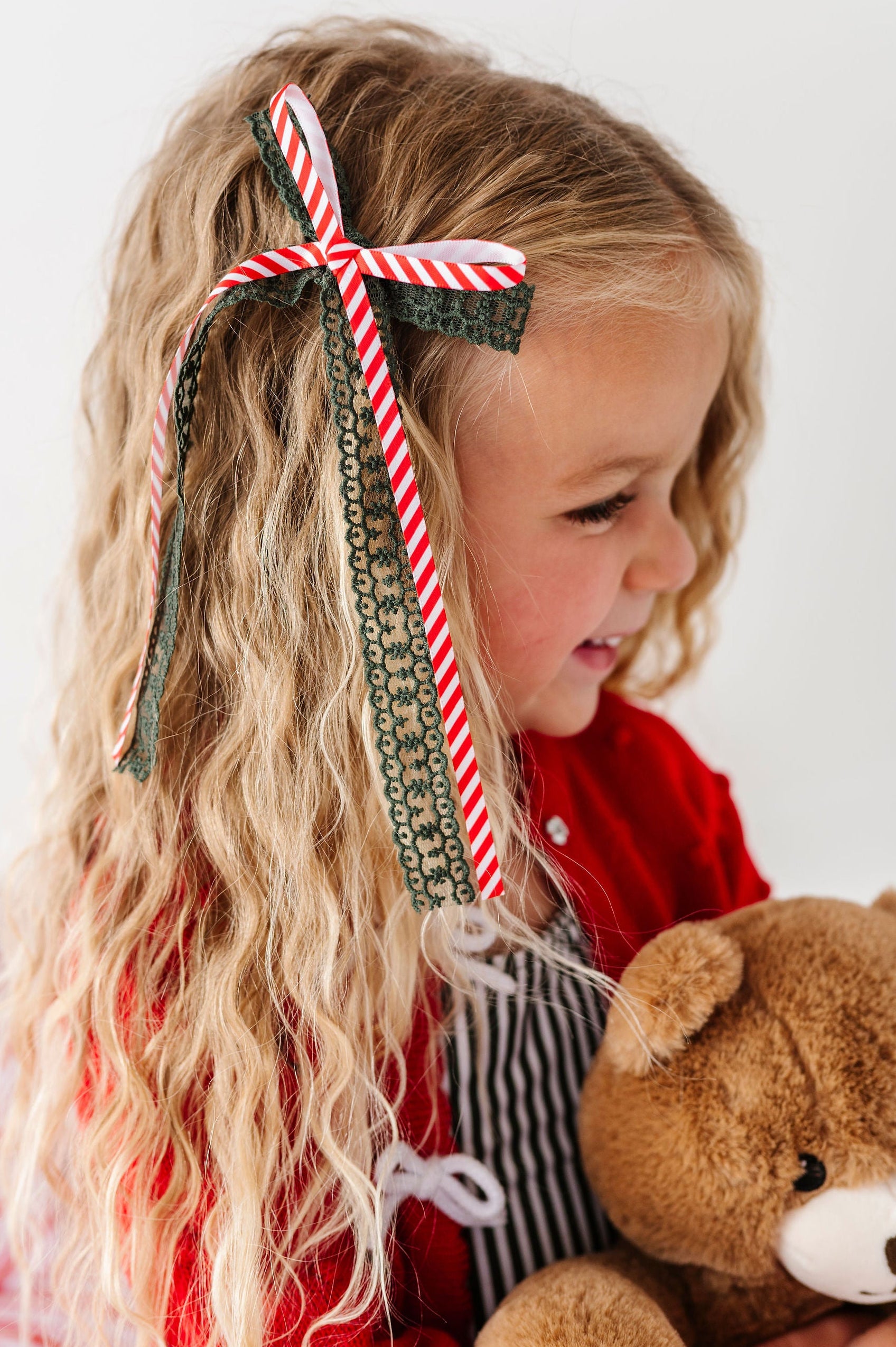 little girl holding teddy bear with candy cane striped and green lace hair bow in her hair
