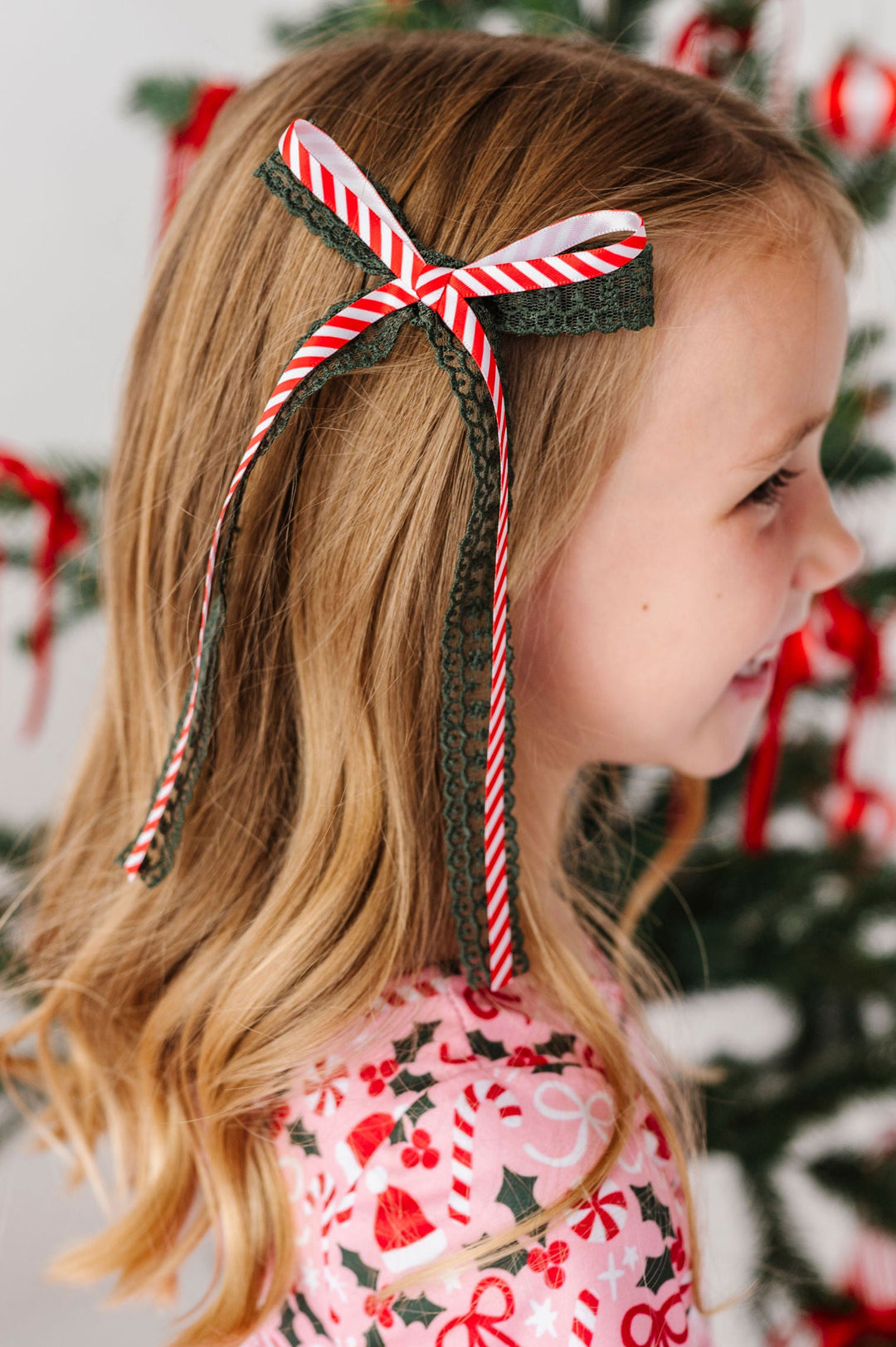 little girl wearing pink xmas dress with candy cane striped and green lace hair bow ribbon in her hair