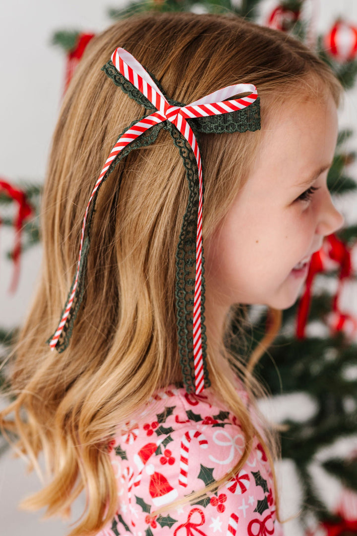 little girl wearing pink xmas dress with candy cane striped and green lace hair bow ribbon in her hair