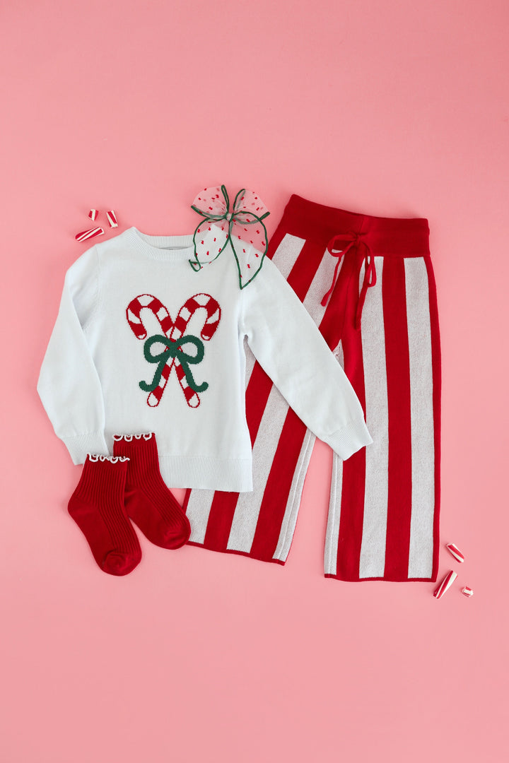 girls candy cane inspired christmas sweater outfit photographed on a solid pink background