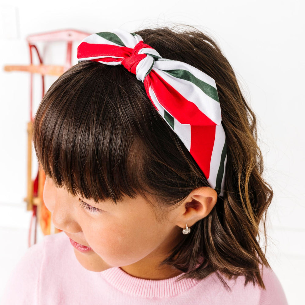 little girl in pink candy cane sweater paired with matching green red and white striped headband bow