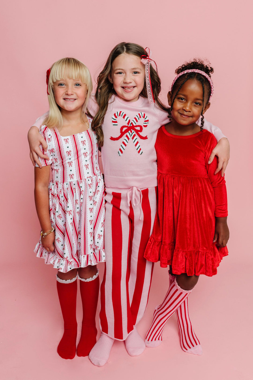 three young girls in mix and match red and pink candy cane sweaters and dresses paired with matching knee high socks and hair bows