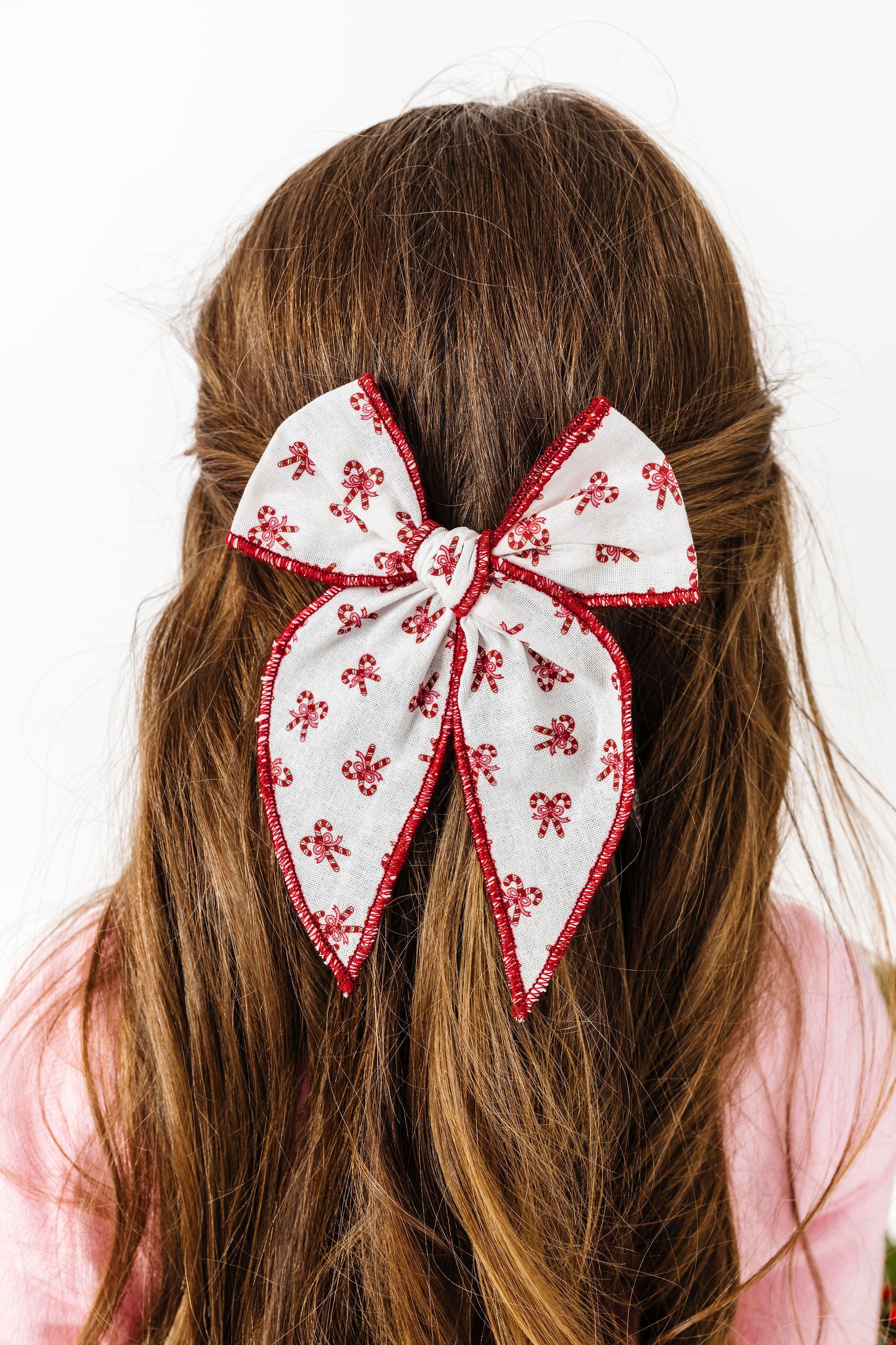girl with hair pulled back in white fabric bow on clip with red trim and red candy cane Christmas print