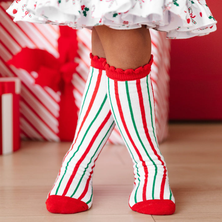 little girl in vintage candy cane knee highs socks with vertical red, white and green stripes and scalloped red border