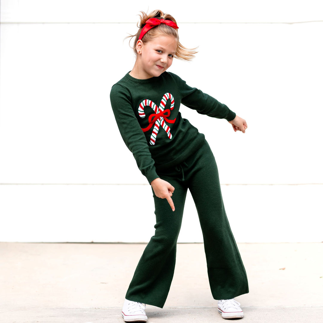 little girl in forest green Christmas pullover with classic candy cane, matching green sweater pants and red satin headband