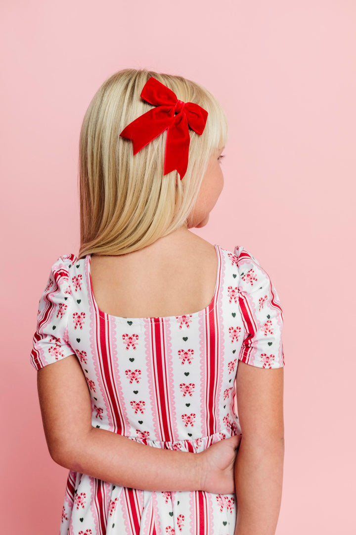 back view of square neck candy cane print twirl dress and matching red velvet ribbon bow on clip