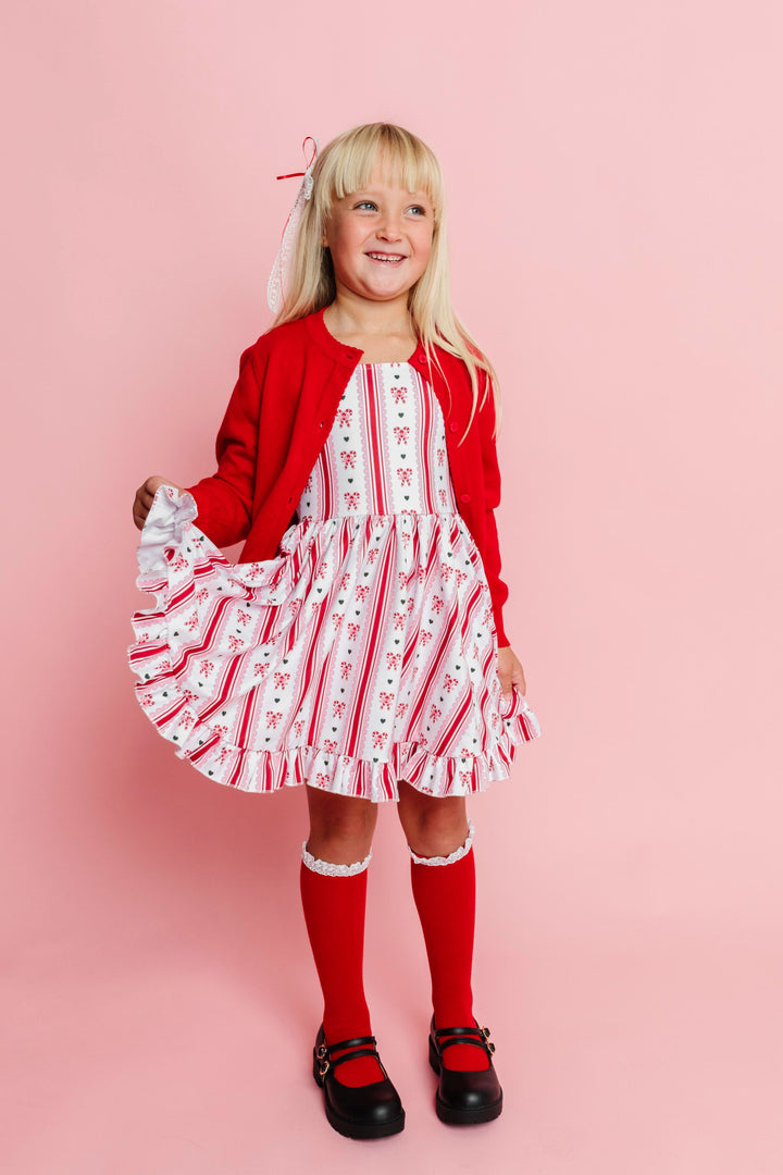 little girl in white Christmas twirl dress with vintage candy cane print in red, pink and green paired with bright red cardigan and matching socks and bow