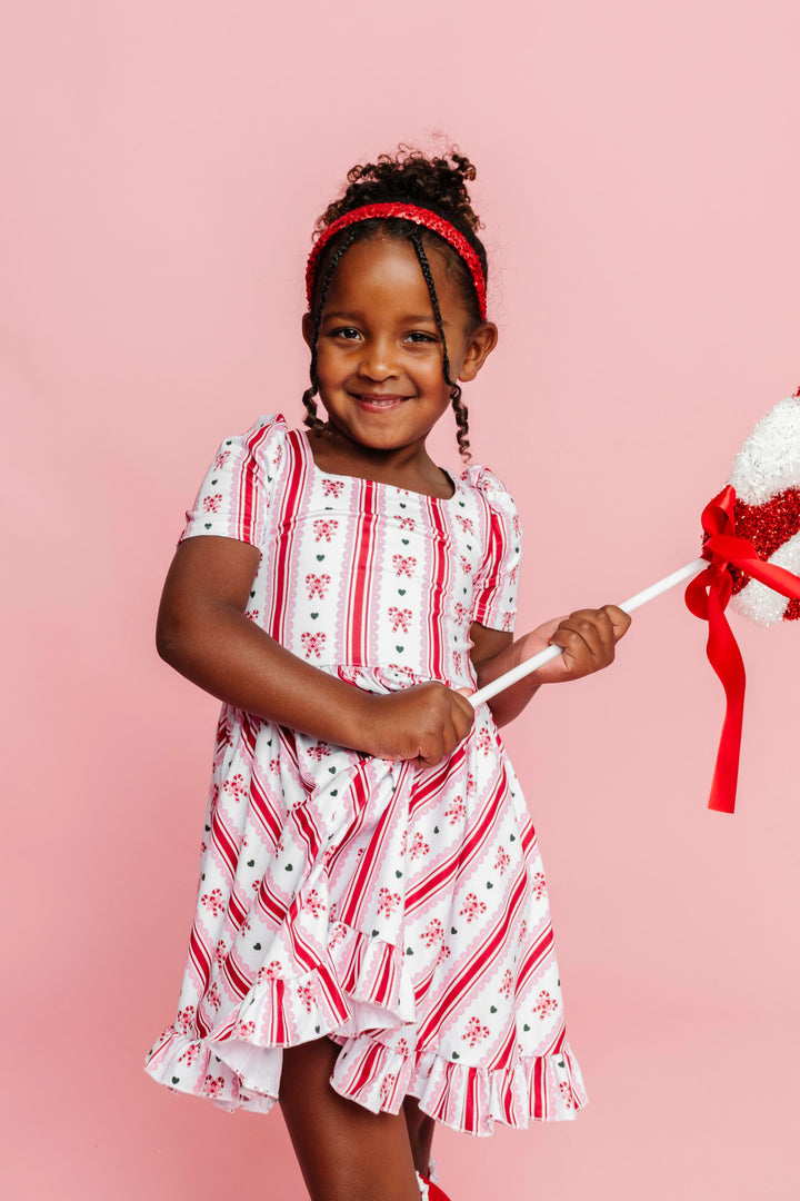 little girl holding peppermint decoration in vintage candy cane print twirl dress and matching sparkly red sequin headband