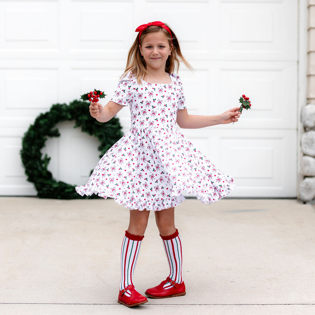 little girl twirling in festive candy cane print dress and matching white, green and red striped Christmas socks and red satin headband