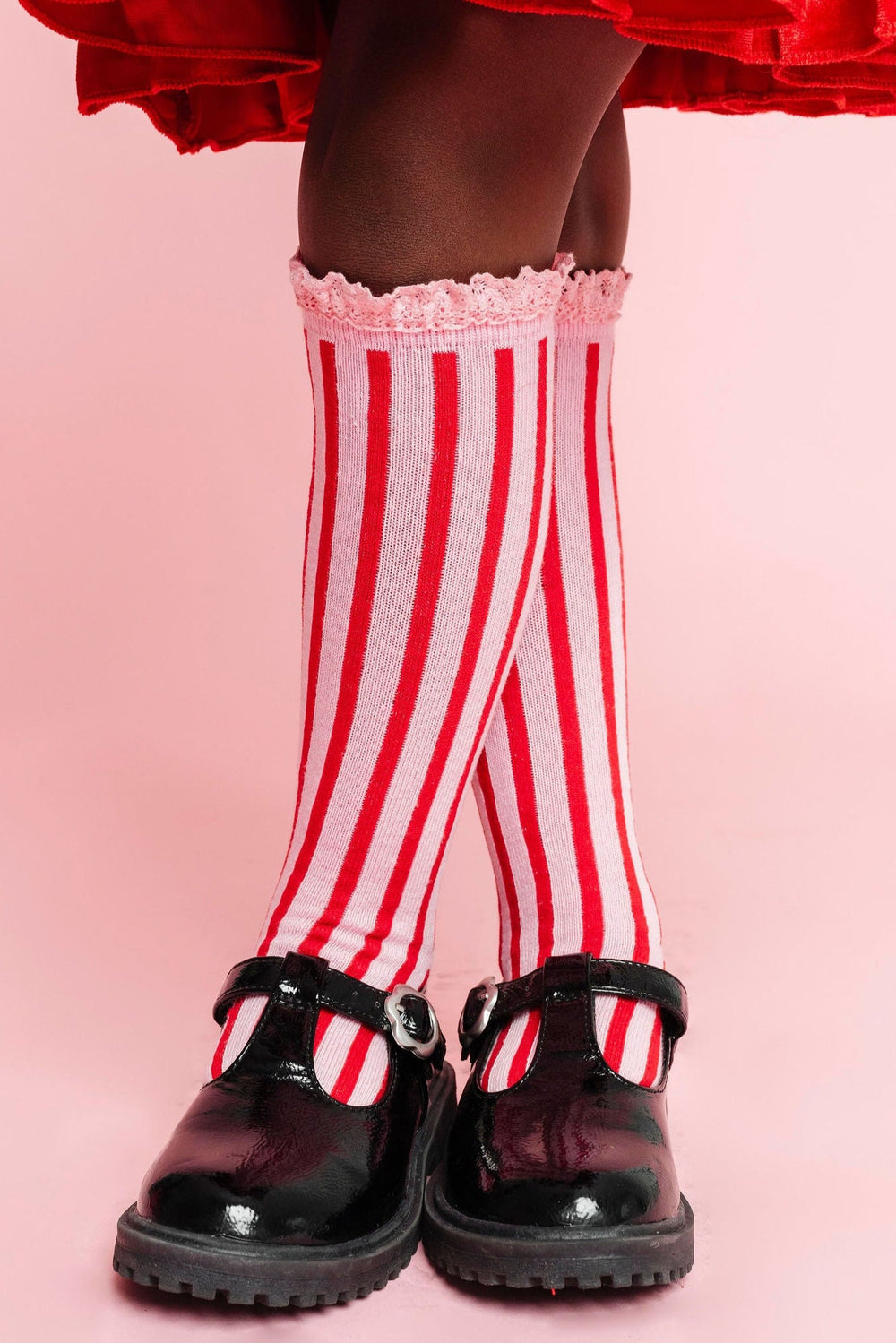 closeup of girl wearing pink lace trim knee high socks with red vertical stripes for Christmas paired with bright red velvet twirly dress