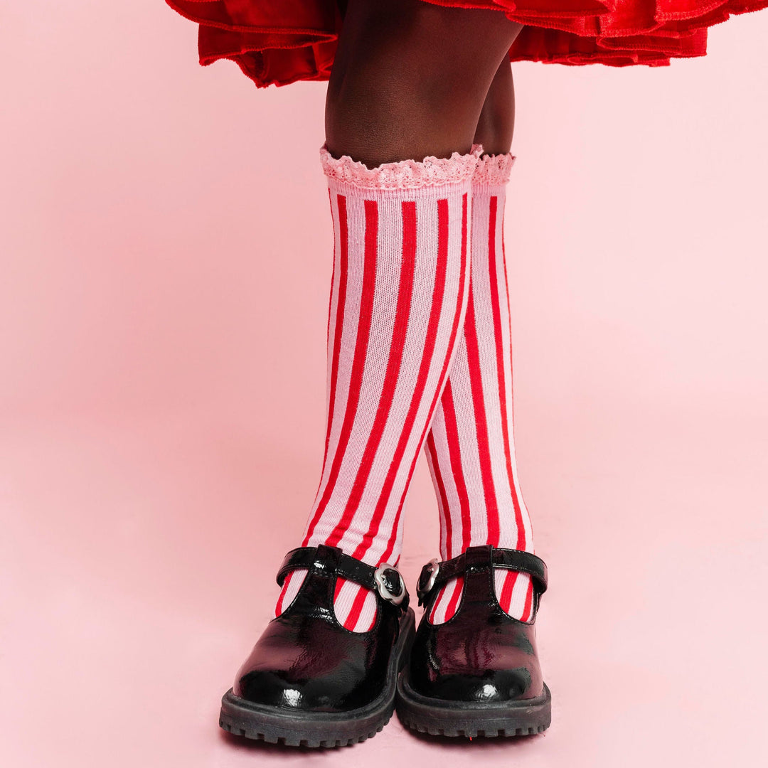 closeup of girl wearing pink lace trim knee high socks with red vertical stripes for Christmas paired with bright red velvet twirly dress