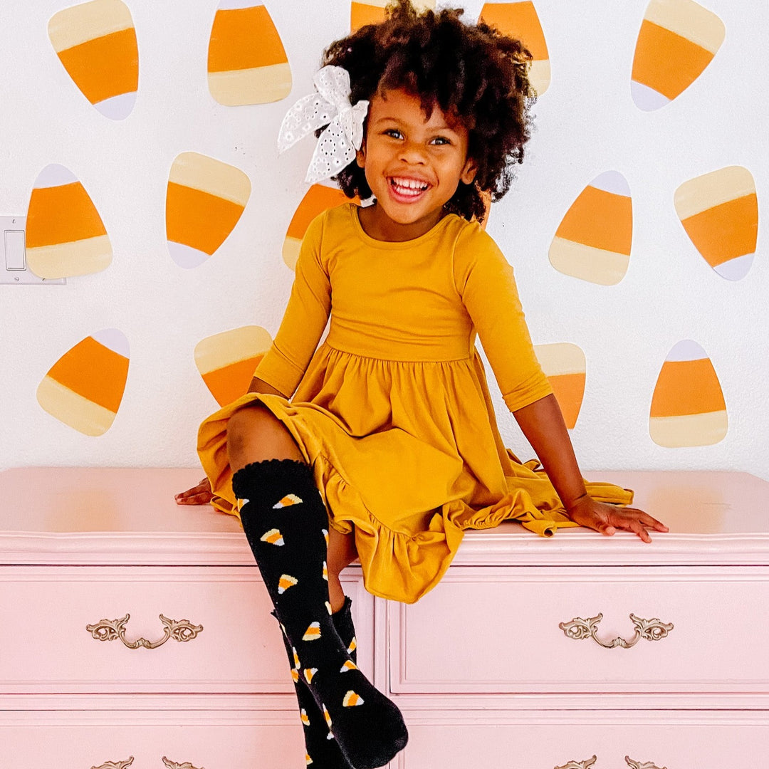 little girl wearing candy corn knee high socks with yellow twirl dress for halloween