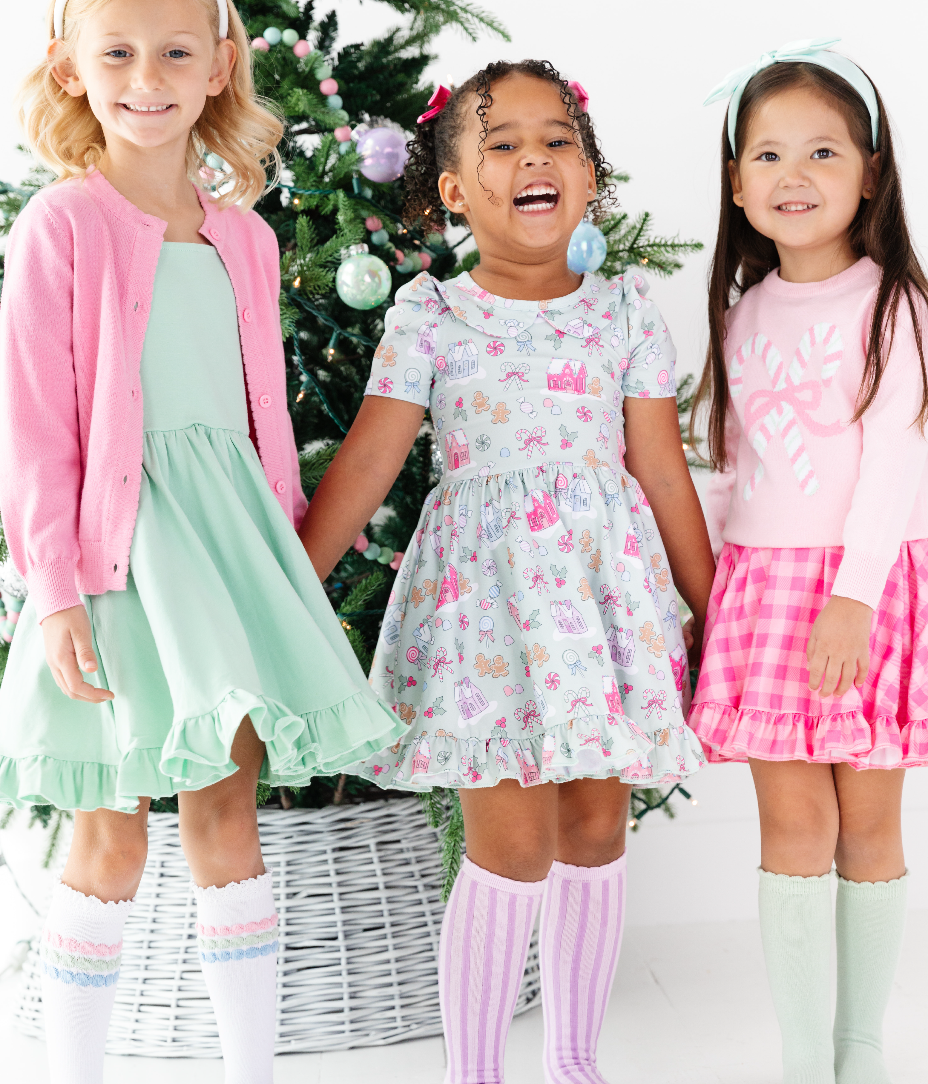 girls standing by tree in Candyland themed pastel dresses and pink sweaters 