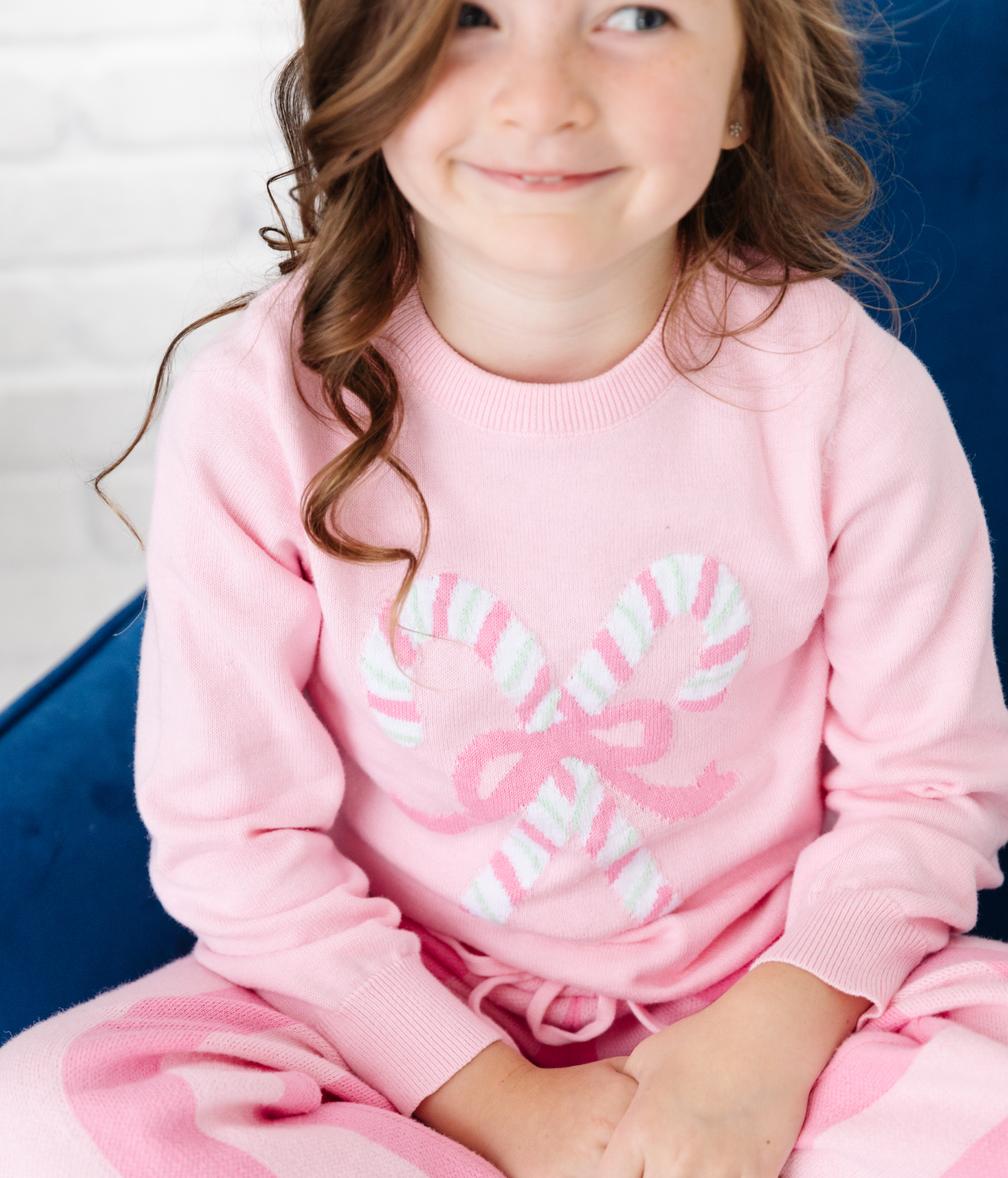 little girl in pastel pink pullover knit sweater with candy cane print for Christmas