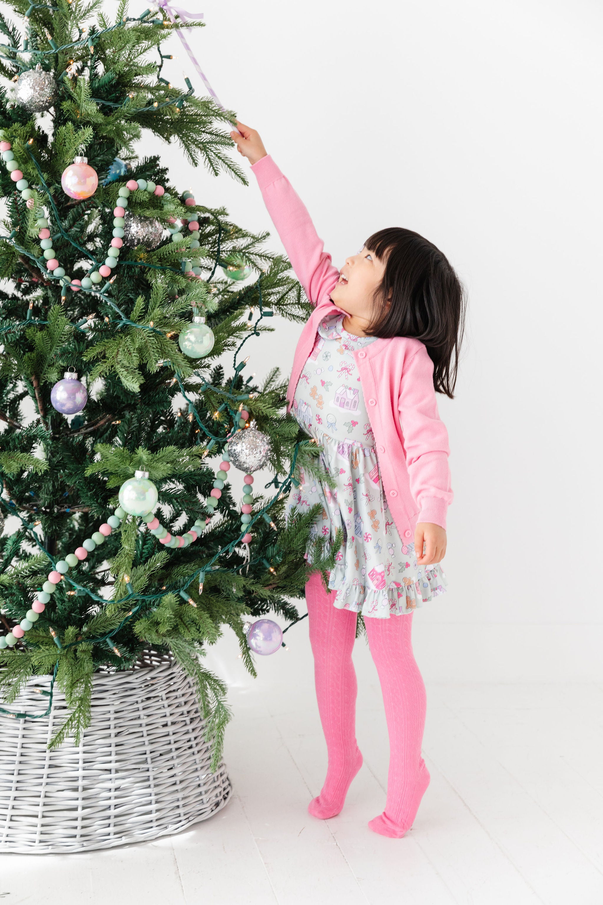 little girl by christmas tree wearing pastel christmas dress with matching pink tights and sweater