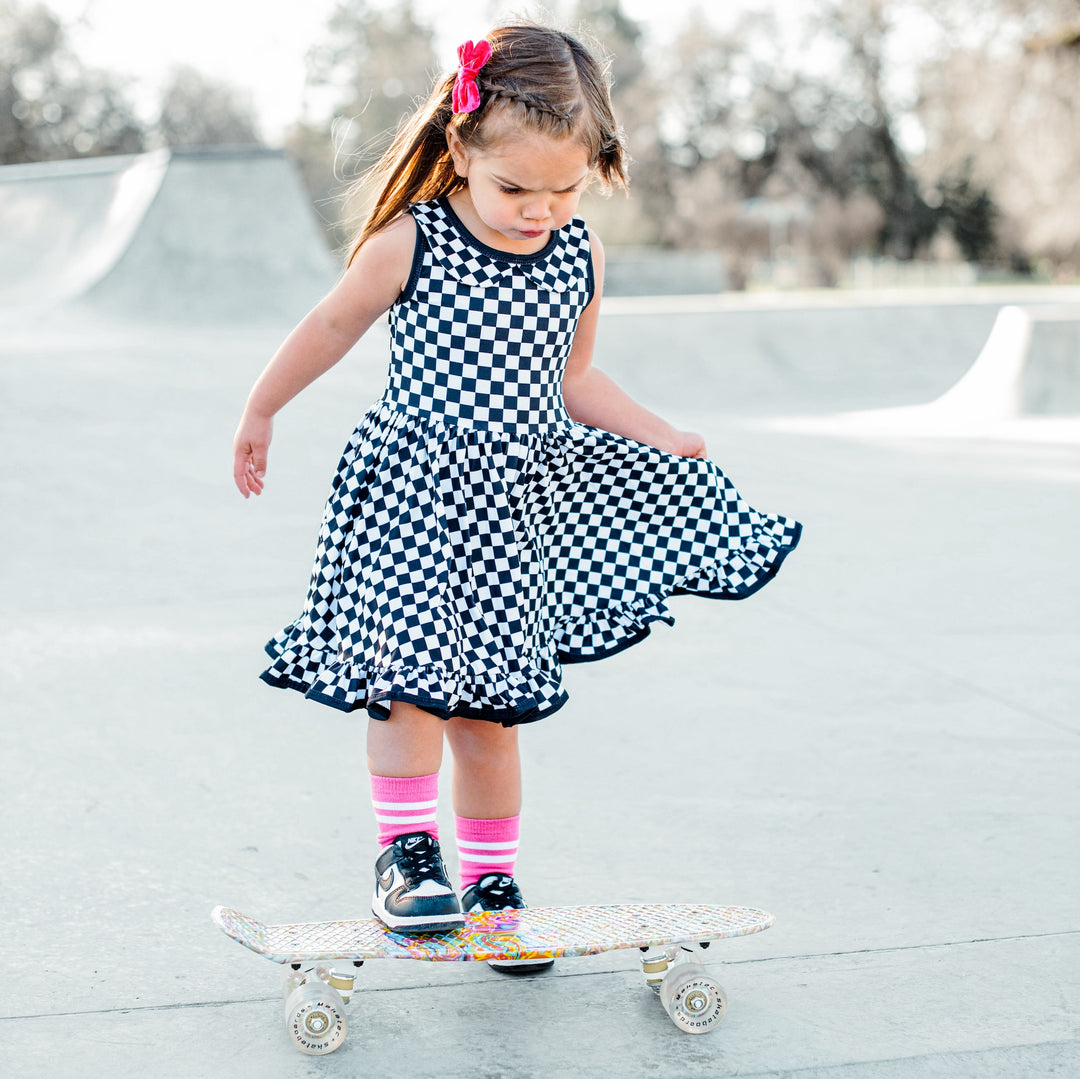 little girl on skateboard wearing black and white chekcered tank top dress and hot pink socks by little stocking co