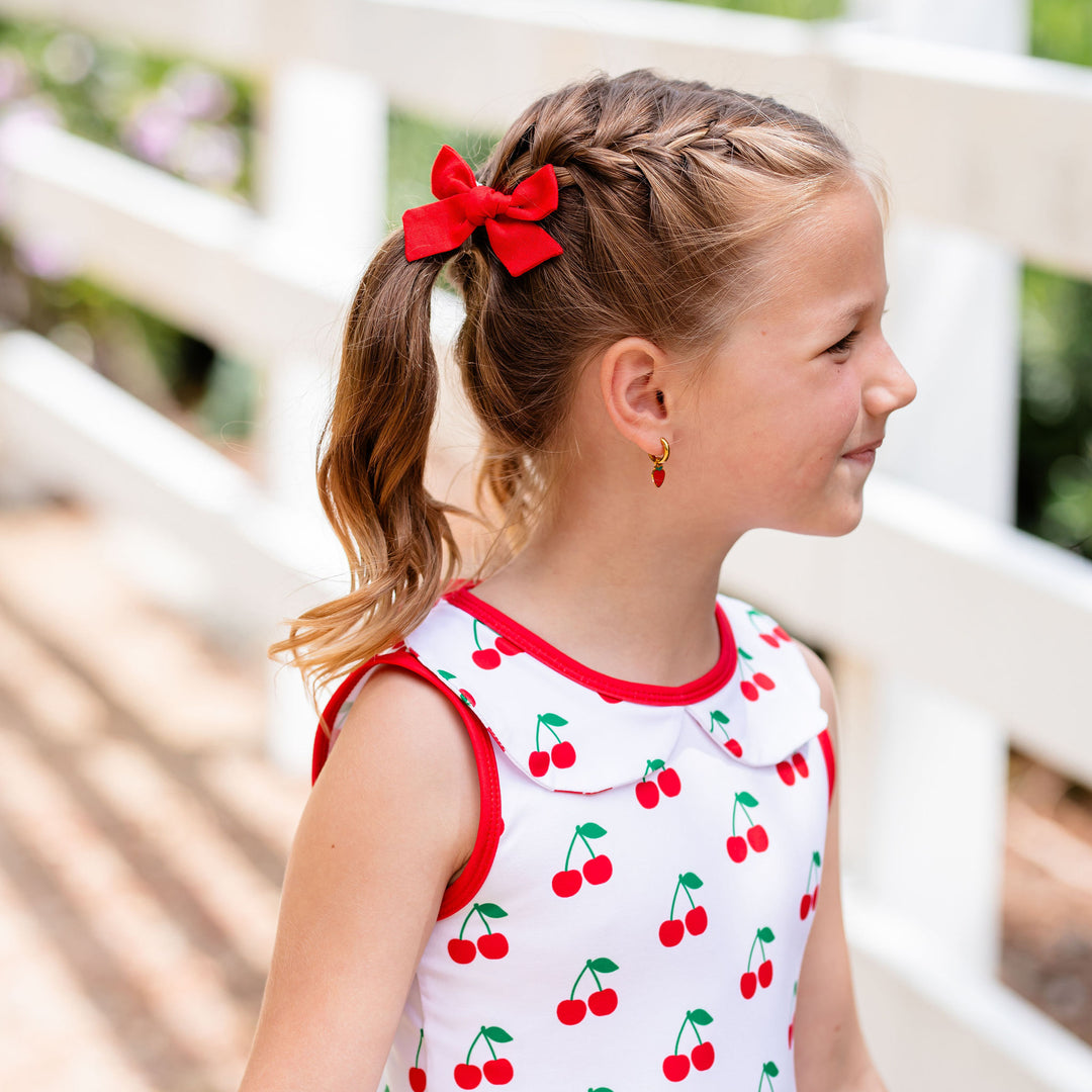 little girl wearing cherry print twirl dress and matching red linen pigtail bows