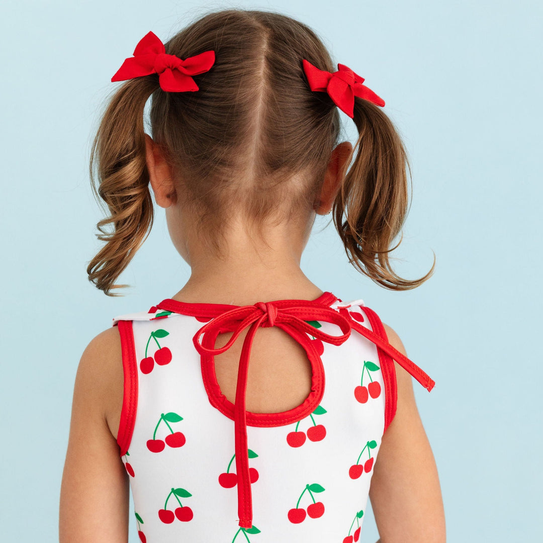 back detail of cherry print twirl dress on little girl wearing pigtails with red linen hair bows