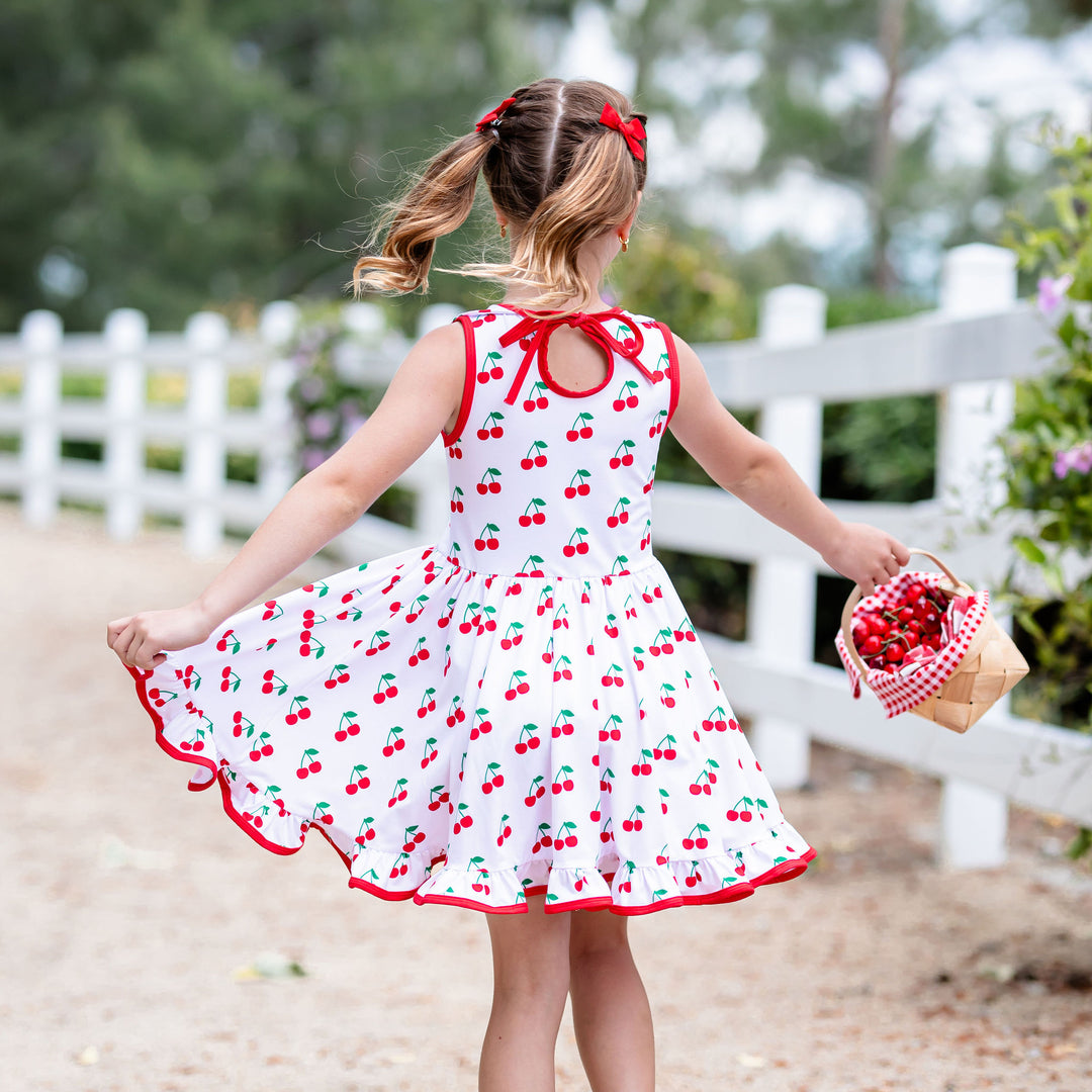little girl twirling in cherry print summer dress holding picnic basket of fresh picked cherries