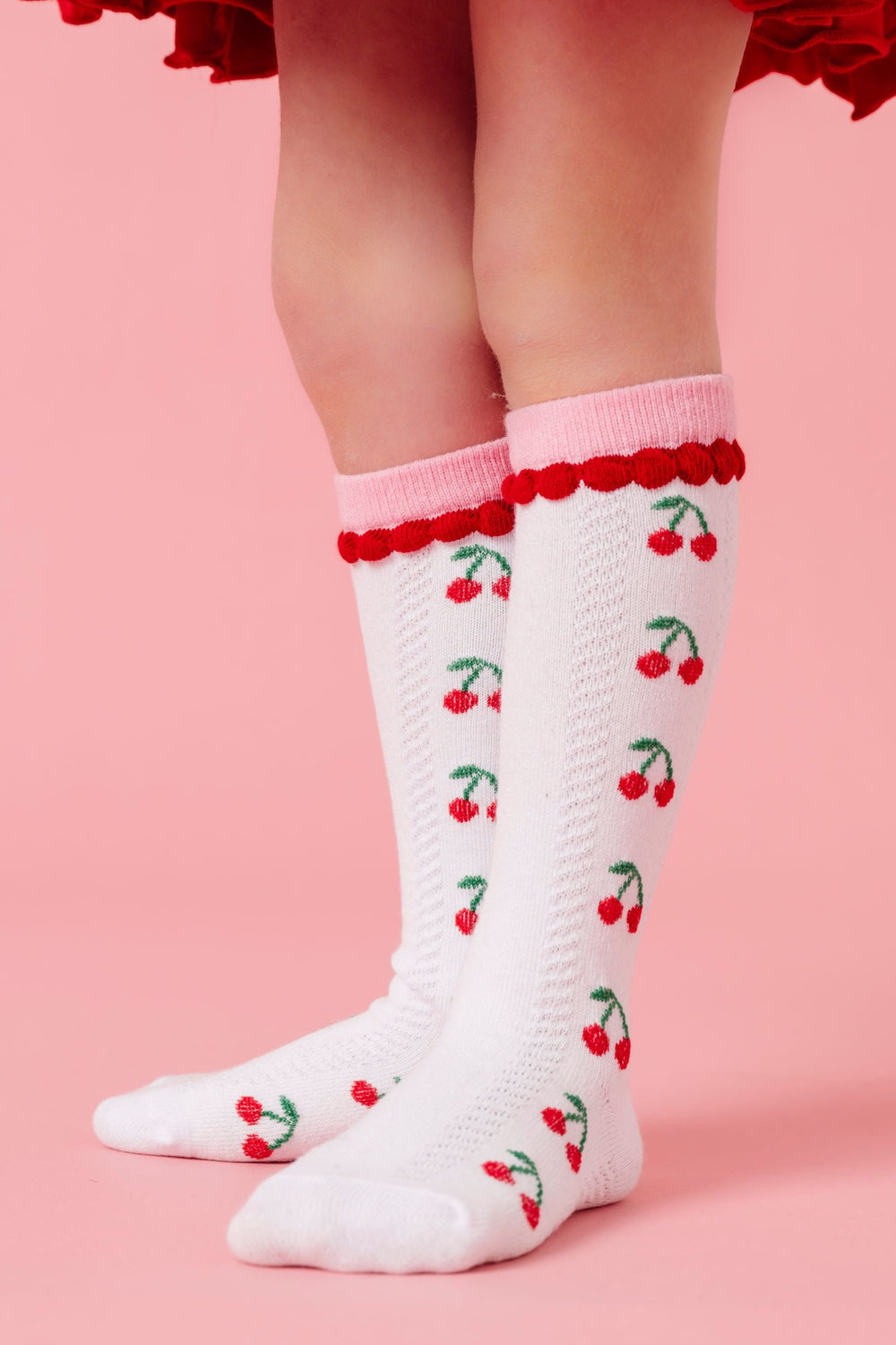 closeup of white cherry print knee high socks with pink and red trim to match cherry themed collection for valentine's day
