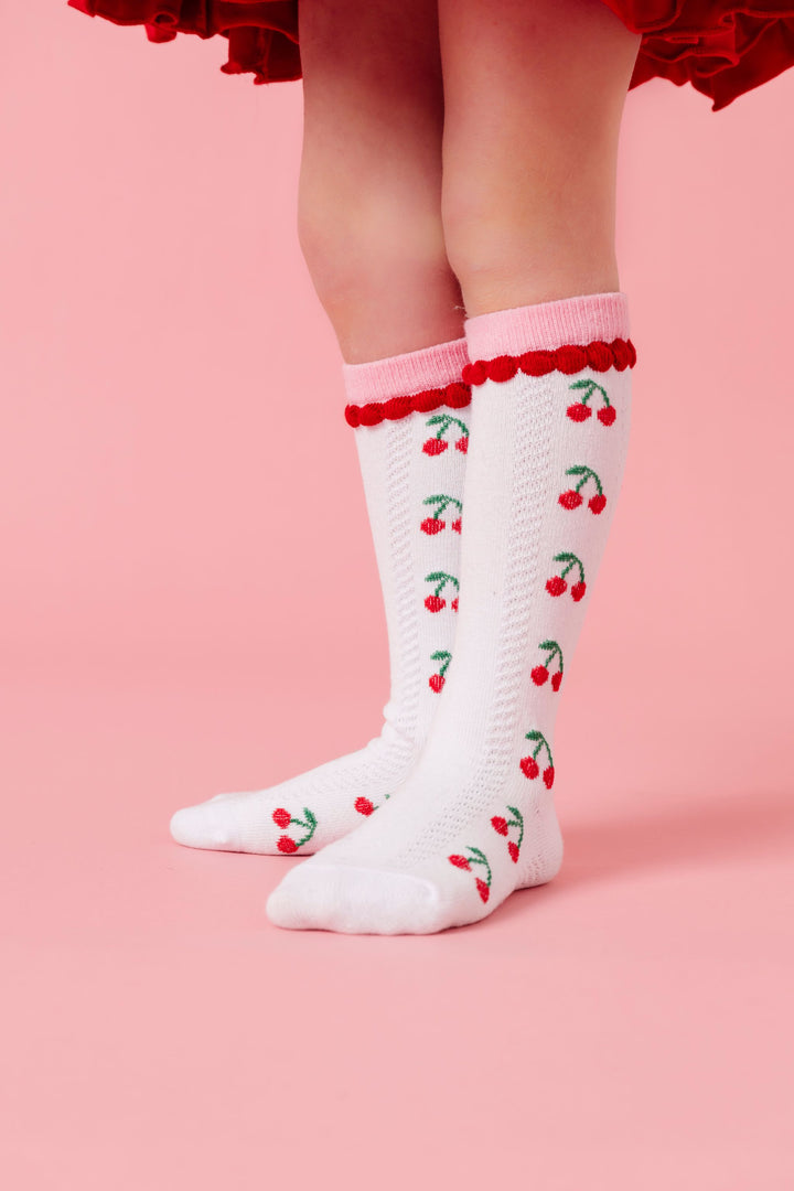 closeup of white cherry print knee high socks with pink and red trim to match cherry themed collection for valentine's day