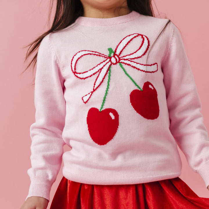 young girl in pink sweater with cherry and bow design paired with bright red velvet skort