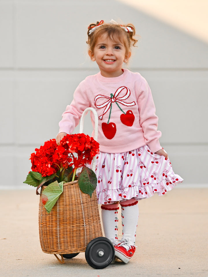 little girl with flower basket and cherry themed outfit including cherry print sweater, dress and socks for Valentine's day