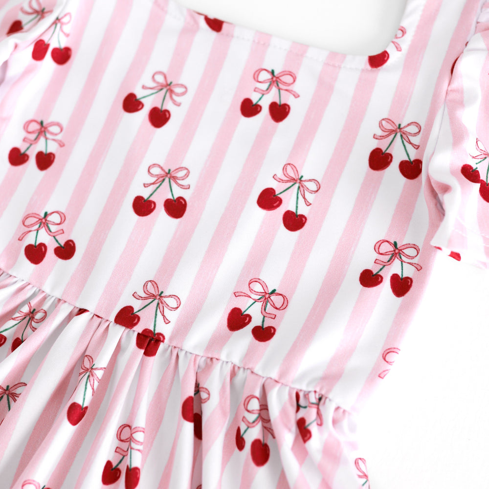 closeup of white and pink striped print twirl dress bodice with ribbon tied cherries
