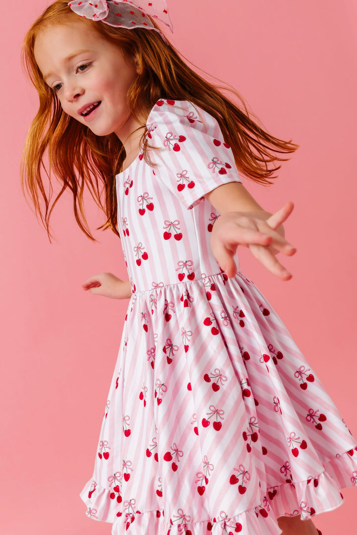girl twirling in pink and white vertical striped twirl dress with ribbon tied cherry print and matching sheer dot bow