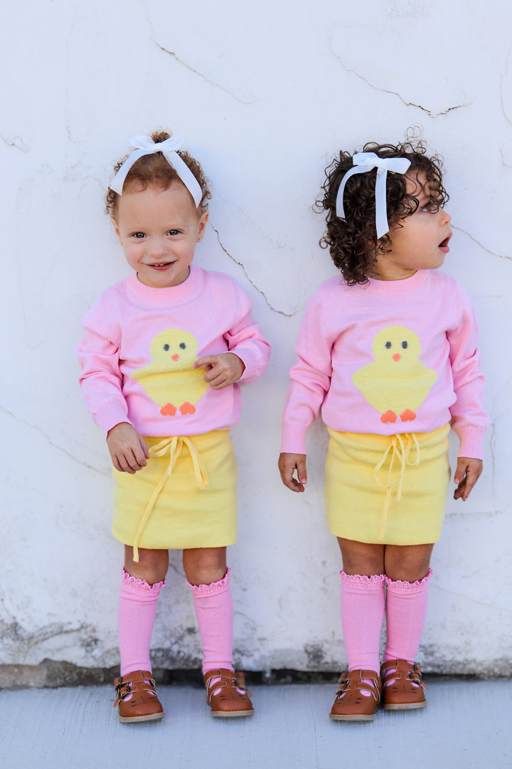 two little girls in cotton knit pink pullover sweater with easter chick and matching yellow skirt, pink knee highs and white velvet long tail bows