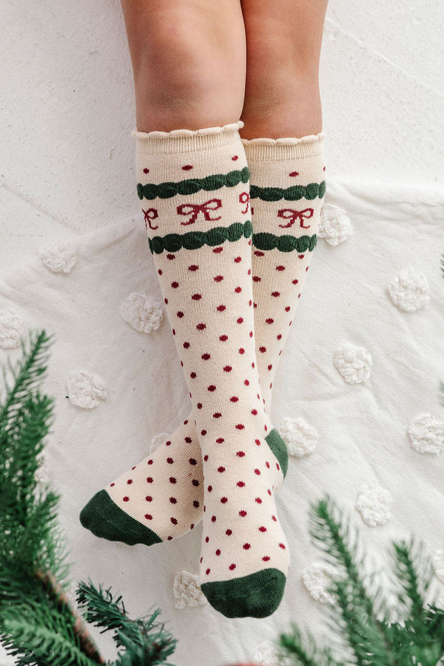 detail photo of girls legs under christmas tree wearing dotted bow knee high socks in christmas colors