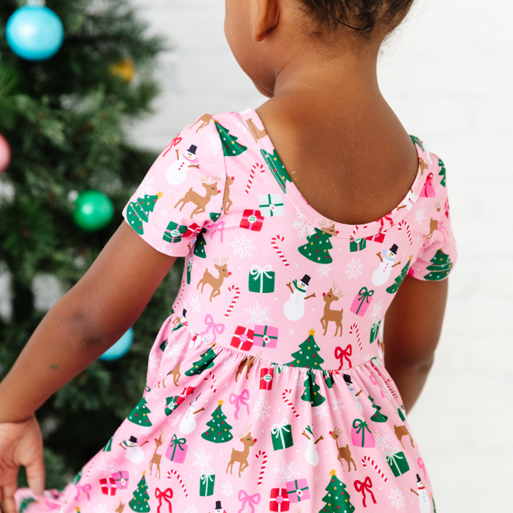 back view of girl wearing pink christmas twirl dress with trees, presents, reindeer and snowmen