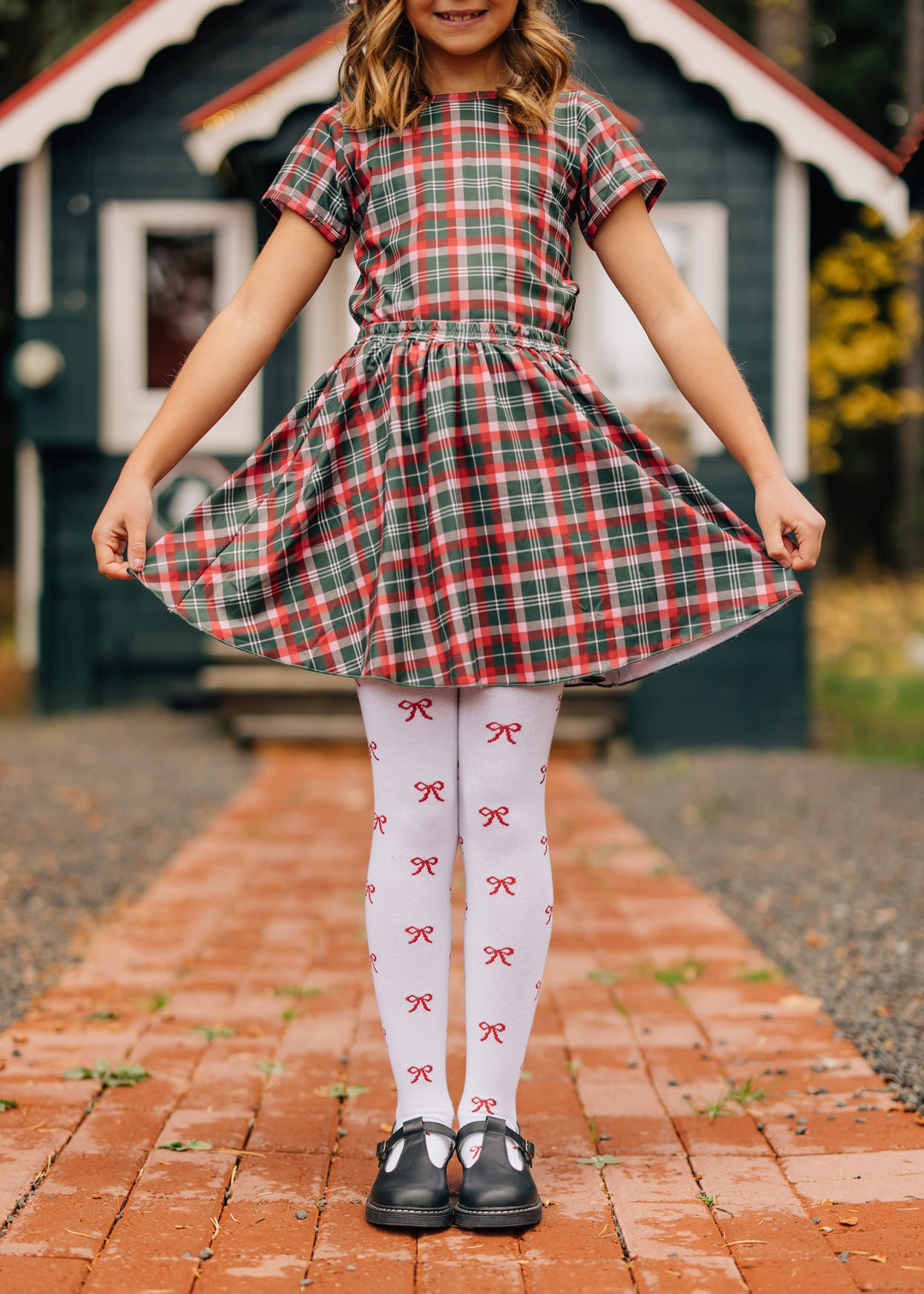 girl in Christmas plaid top and skirt set with white knit tights with red bow design and black mary janes