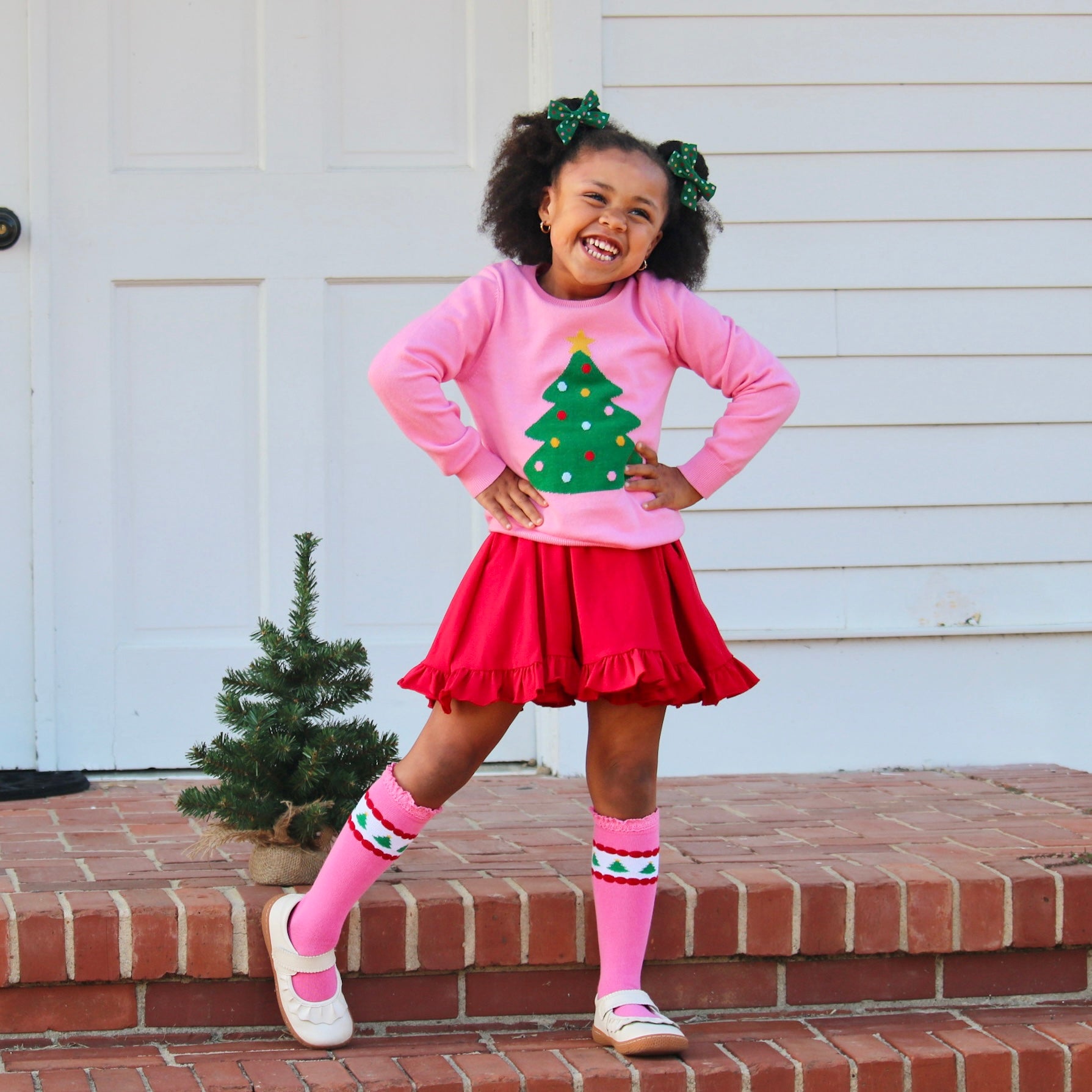 girl in christmas outfit with red twirl dress, pink christmas tree sweater and matching knee high socks