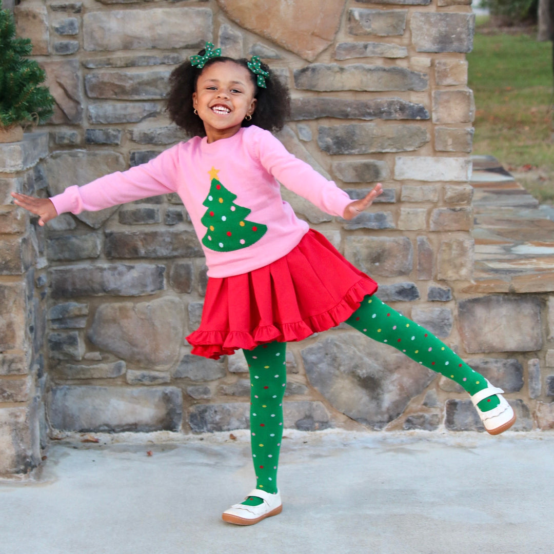 girl in christmas outfit with red twirl dress, pink christmas tree sweater and matching tights and bows