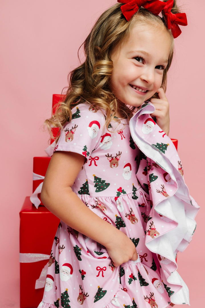 little girl in festive Christmas party themed twirl dress with pink background paired with bright red velvet pigtail bows on clips