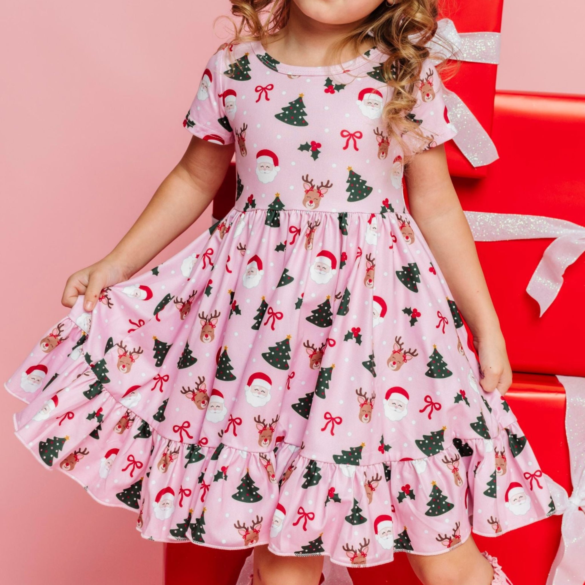 little girl wearing pink short sleeve twirl dress with classic Santa, reindeer, and Christmas tree print