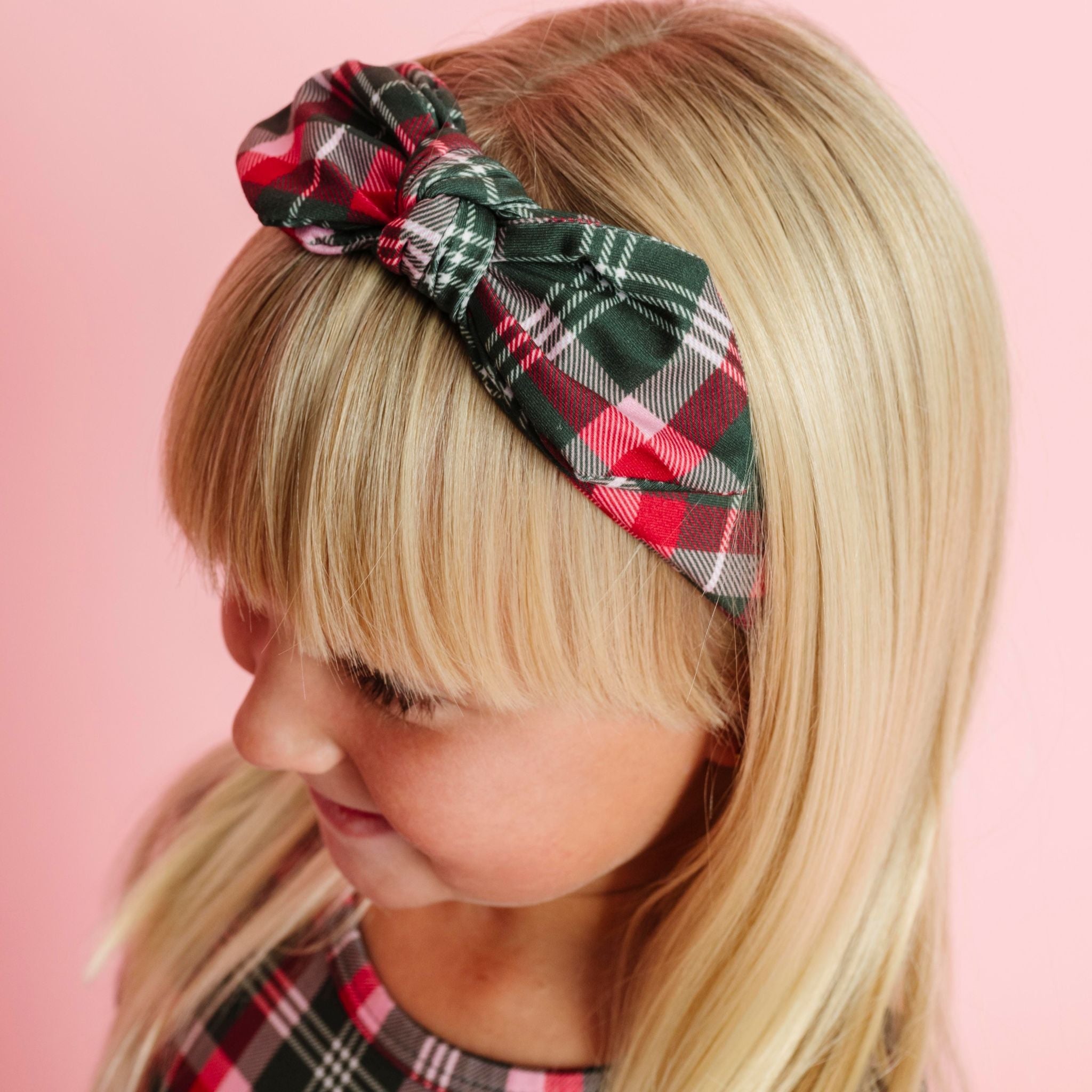 little girl in green, pink and red plaid bow headband paired with matching plaid Christmas top