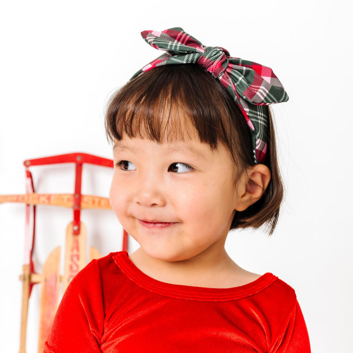 little girl standing in front of sled in Christmas plaid headband with matching bright red velvet top