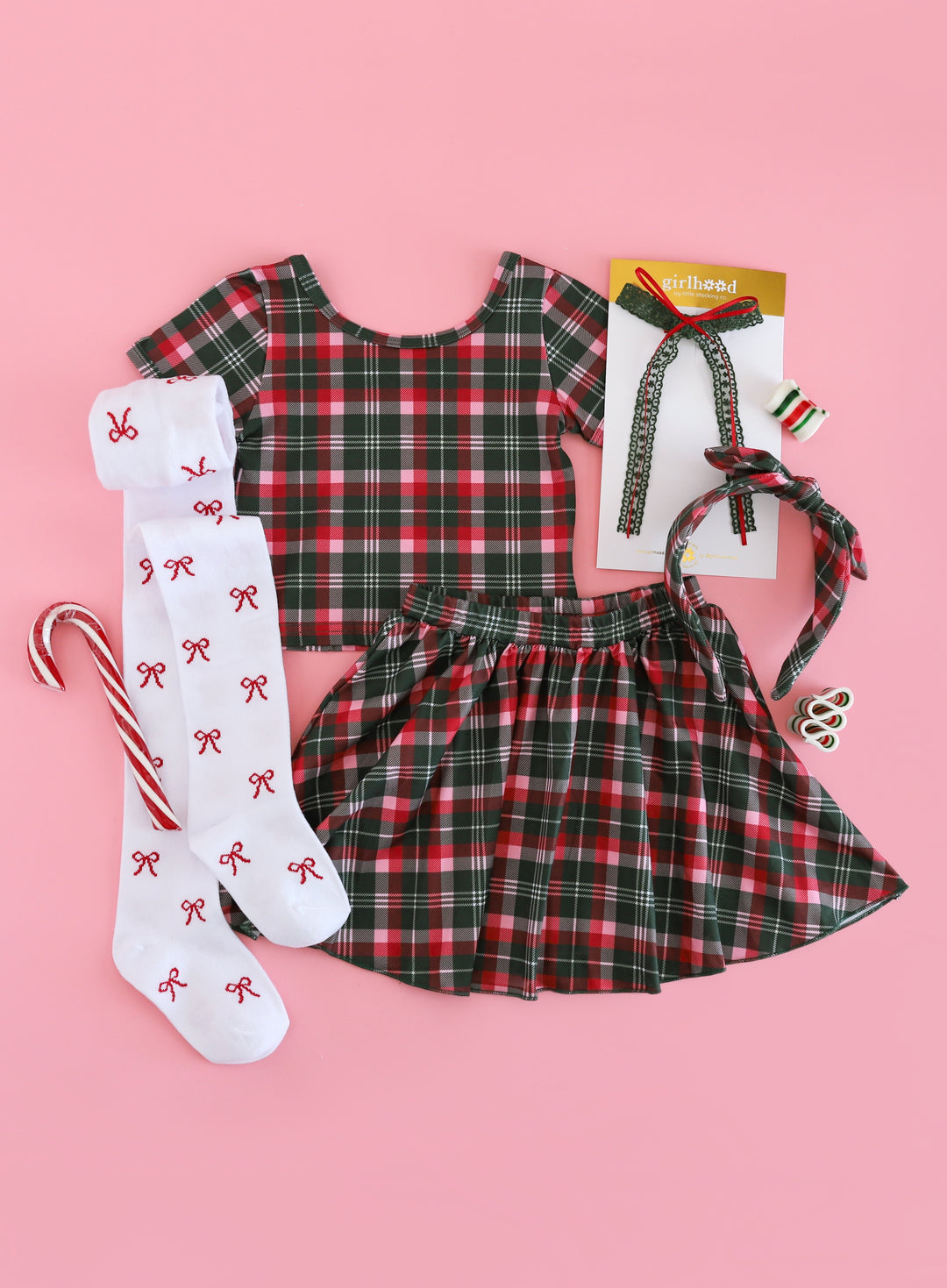 flat lay of girls red, green and pink plaid top and skirt with matching plaid headband, forest green lace bow and red bow tights