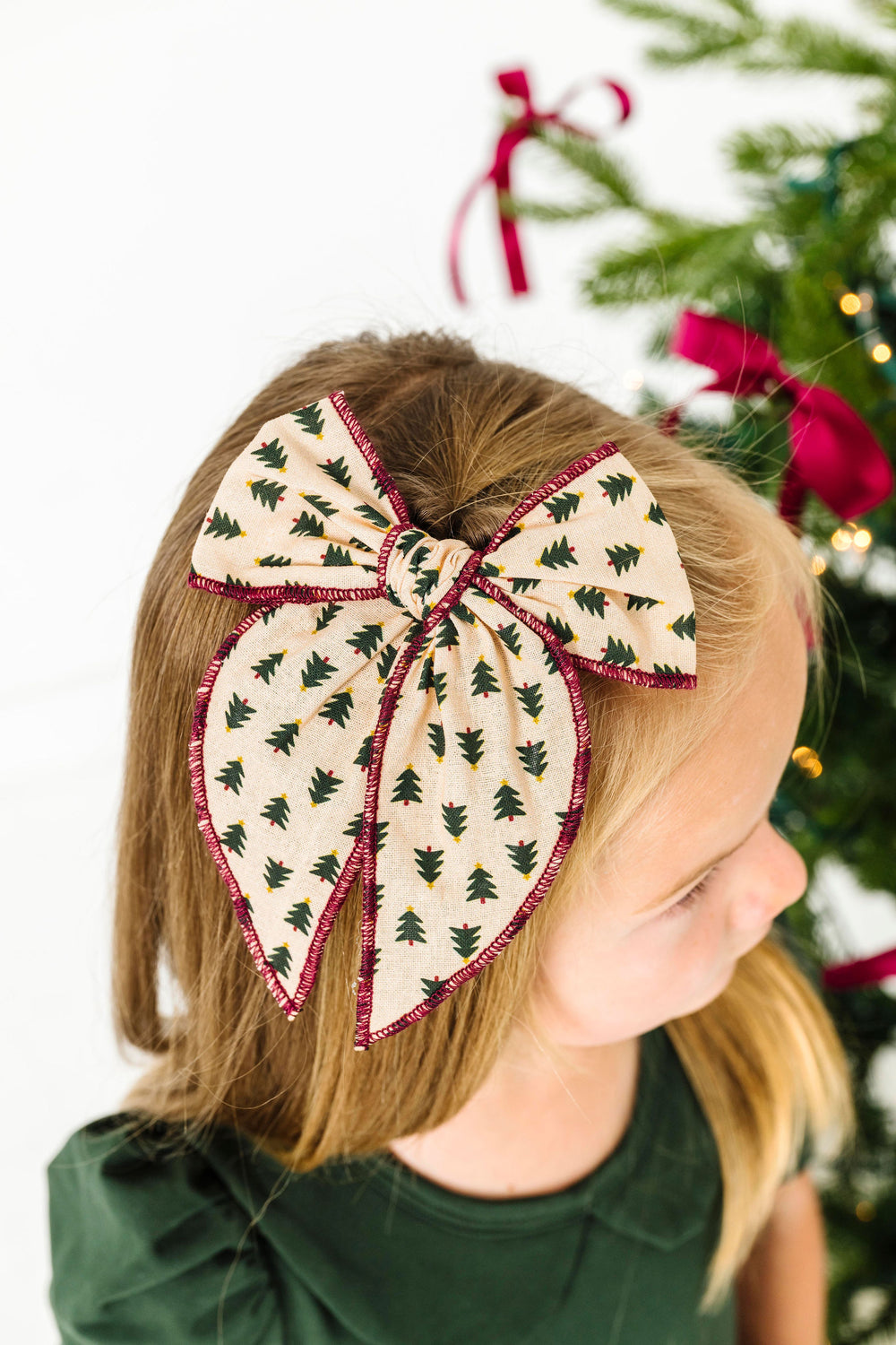 girl in cream fabric hairbow on clip with green Christmas tree design and red trim
