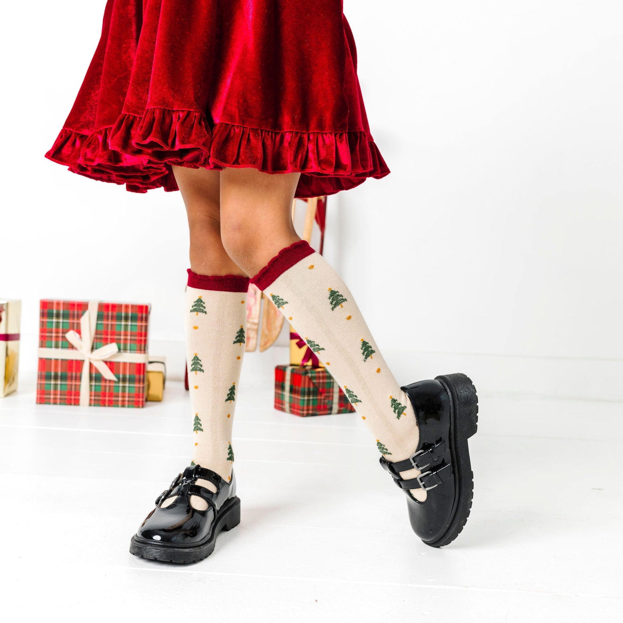little girl in cream knee socks with Christmas tree design and crimson scalloped trim paired with matching crimson velvet twirl dress