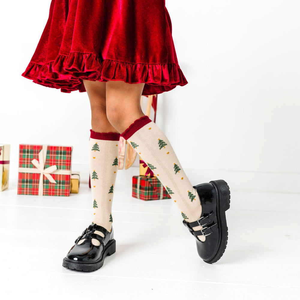 little girl in cream knee socks with Christmas tree design and crimson scalloped trim paired with matching crimson velvet twirl dress