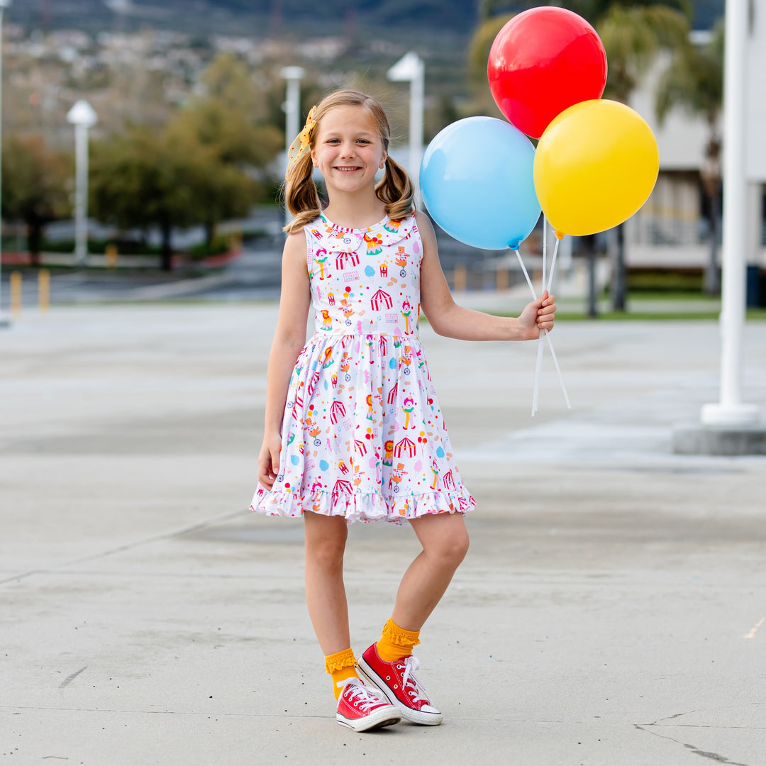 little girl holding balloons wearing circus inspired summer dress