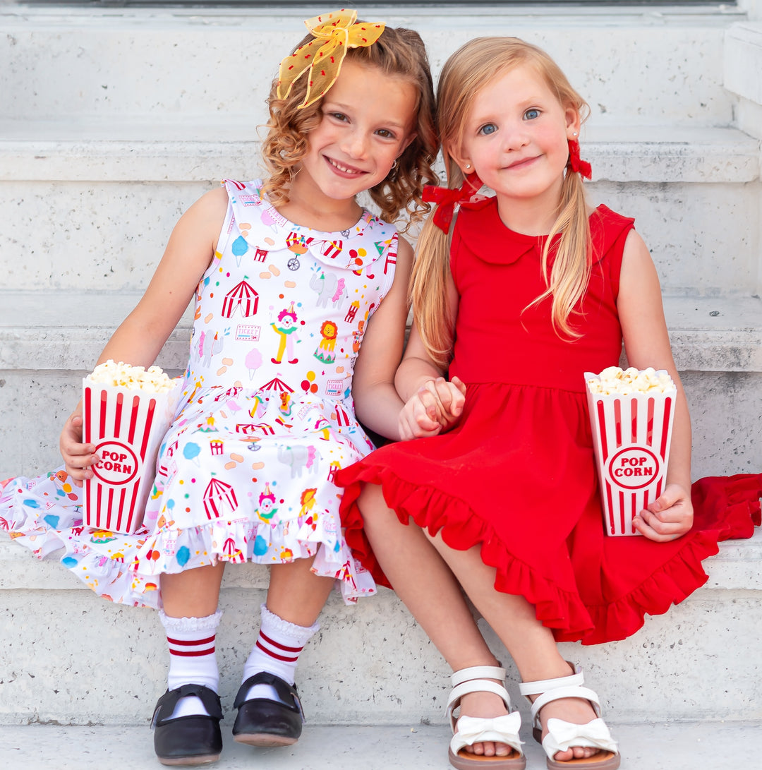 two girls sitting on steps in circus themed twirl dresses eating popcorn