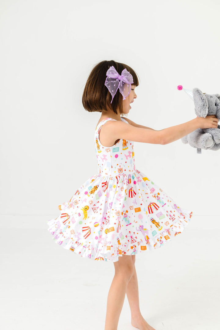 little girl twirling with stuffed elephant toy in circus themed twirl dress featuring characters, animals and treats for a day at the fair